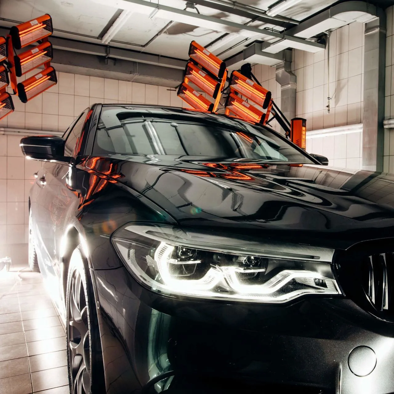 Black car under infrared drying lamps in a garage.